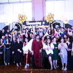 Group of people dressed in formal attire posing for a photo in front of a stage with a "Championship in Dancing Excellence" sign and balloons.