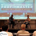 Two men seated on a stage during the 10th Anniversary Conference 2024 of ProfitMaster in Clark, Pampanga. A screen behind displays event details. Audience members are partially visible in the foreground.