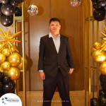 A man in a suit stands in front of a decorated archway with gold stars and black and gold balloons. The URL "www.profitmaster.com.au" is visible at the bottom.