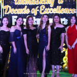 A group of eight people dressed in formal attire posing in front of a decorative backdrop that reads "Celebrating a Decade of Excellence".