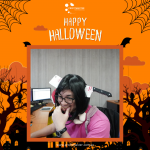 Person wearing glasses and a pink shirt with a Halloween decoration of a fake knife through the head. Background has "Happy Halloween" text and spooky illustrations.