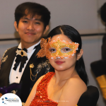 A woman in an orange sequin dress and butterfly mask sits in the foreground, with a smiling man in formal attire behind her. The image includes a logo for Profitmaster and a website URL at the bottom.