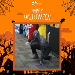 Person in a black Spider-Man costume crouching on a carpeted floor, surrounded by Halloween-themed graphics and the text "Happy Halloween.