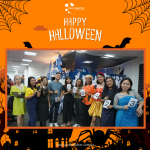 A group of people in costumes holding number cards, standing in front of a Halloween-themed backdrop.