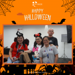 Four people in costumes pose together, with a "Happy Halloween" banner above them and an orange, Halloween-themed border.