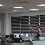 A man stands with raised arms in a busy office with multiple employees working at desks.