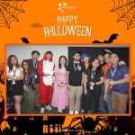 Group of people in Halloween costumes posing for a photo, with a "Happy Halloween" banner above them and decorative borders.