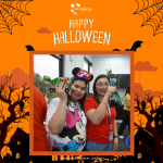 Two people posing with Halloween decorations in front of an orange background with bats and trees. The image says "Happy Halloween" at the top.