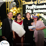 A group of four people, two men and two women, posing in front of a decorative backdrop that reads “Decade of Excellence, Profitmaster 10th Anniversary.” One woman is holding a voucher and wearing a mask.