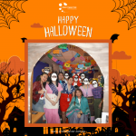 Group of people in Halloween costumes poses in a decorated setting with a "Happy Halloween" sign above them.