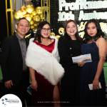 Four people dressed formally, standing in front of a backdrop with balloons and the text "Profitmaster 10th Anniversary." One person holds an envelope labeled "Aqua Planet.