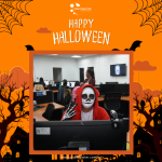 Person in a skeleton face paint and red hooded outfit flashes peace signs in an office decorated with Halloween elements.