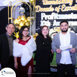 Four individuals posing in front of an 'Unmasking a Decade of Excellence' backdrop, with one person holding a Goth Kitchen & Bar voucher. The event appears to celebrate Profitmaster's 10th anniversary.