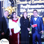 Four individuals, three in formal wear and one in a suit, stand together at an event with a backdrop reading "Decade of Excellence: Profitmaster's 10th Anniversary.