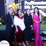 A group of four people posing for a photo at an event with a "Profitmaster 10th Anniversary" backdrop. One person is holding a red envelope.