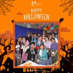 A group of people posing for a Halloween-themed photo, some in costumes, with festive decorations in the background.