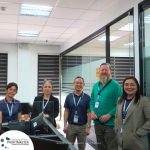 A group of five people, wearing office attire and lanyards, stand in a modern office space. A logo in the bottom left corner reads "PROFITMASTER Global Outsourcing.