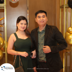 A man and a woman standing together, dressed formally, at an event with gold and black decorations.