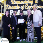 Five people stand on a stage with "Unmasking a Decade of Excellence" backdrop. One in the center holds a certificate. All wear formal attire, with some wearing masquerade masks.