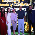 A group of six people in formal attire, some wearing masks, posing in front of a backdrop at an event celebrating a decade of excellence.