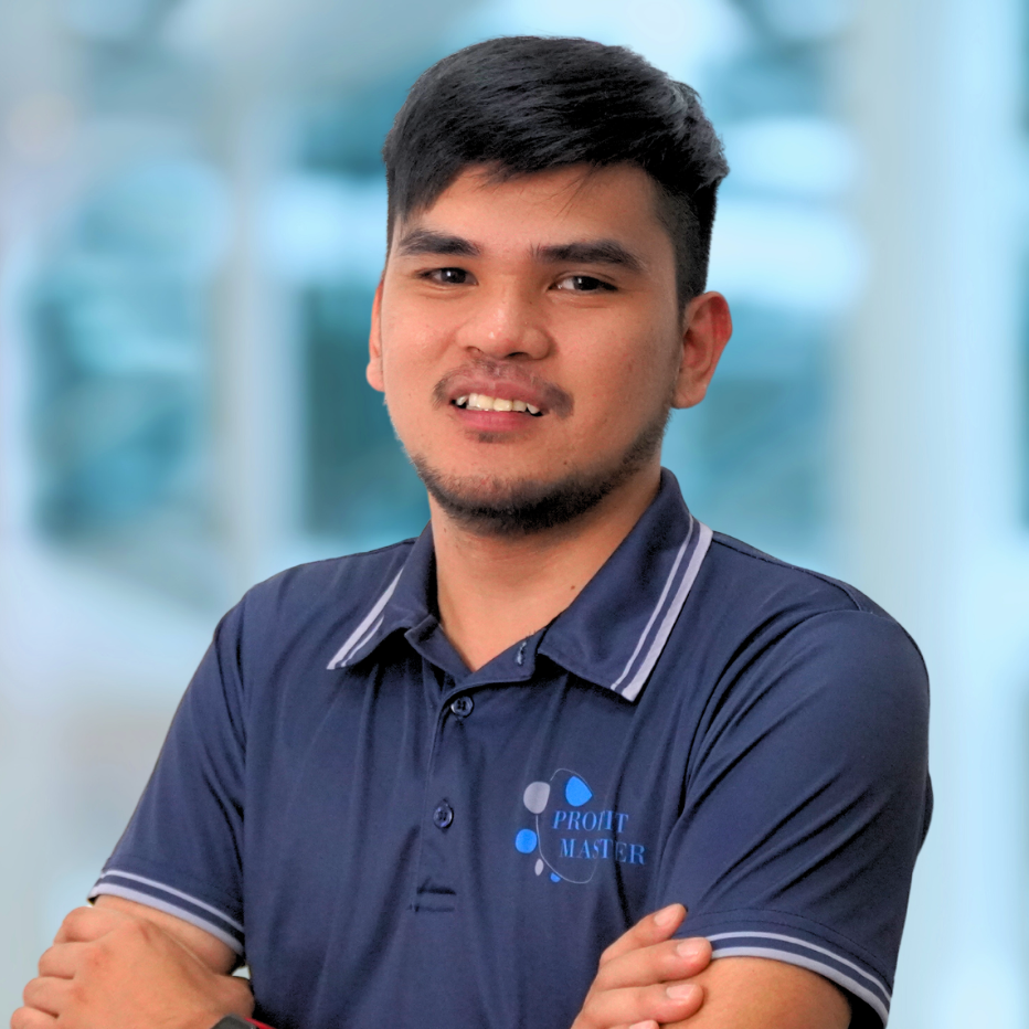 A member of our team with short dark hair and a trimmed beard is wearing a dark blue shirt featuring the "Profit Master" logo, standing with arms crossed against a blurred background.